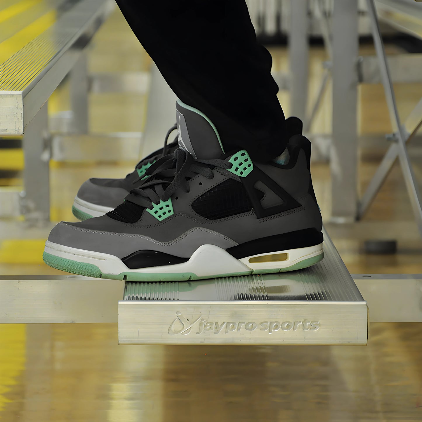 Person wearing black and green sneakers standing on aluminum bleachers.