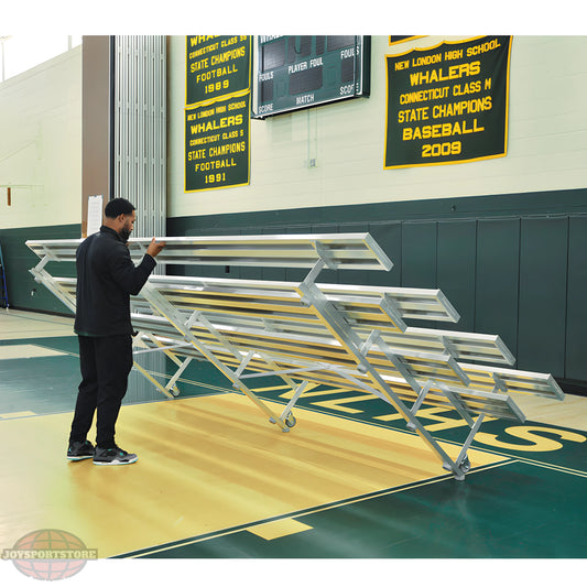 Man folding metal bleachers in gym with championship banners displayed.