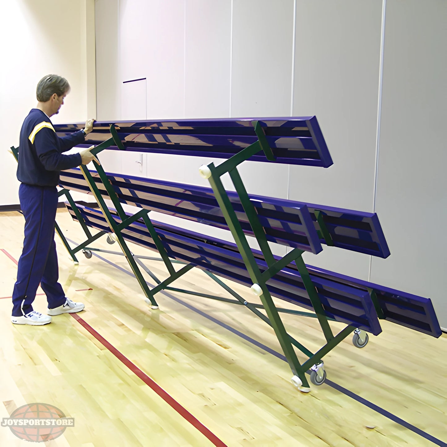 Man folding indoor bleacher seats with green frame and wheels.