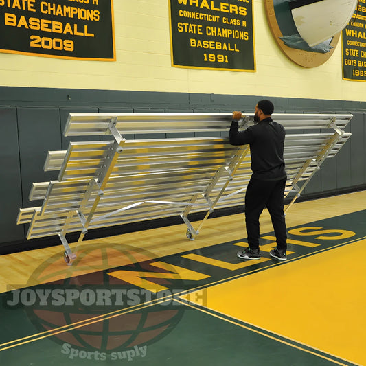Man folding metal bleachers in gym with championship banners displayed.