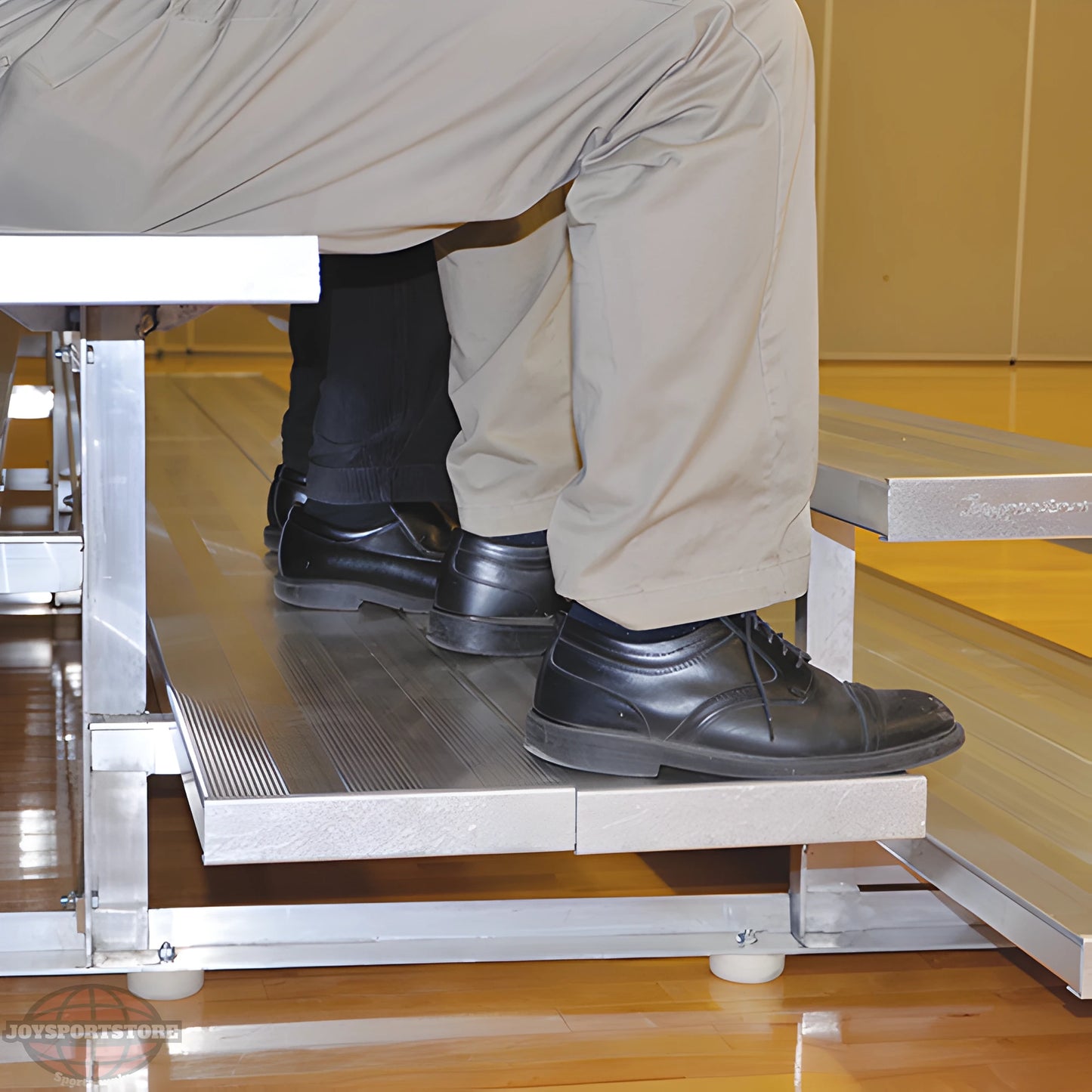 Person wearing sneakers sitting on indoor bleacher seats with aluminum frame.