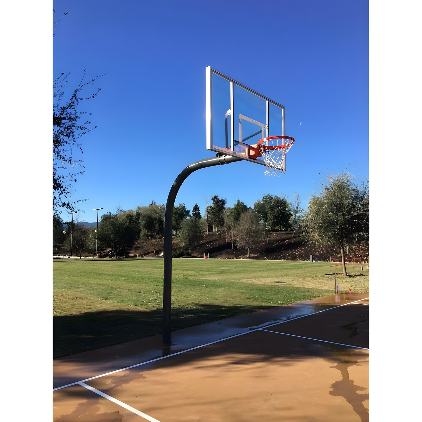 Gared outdoor basketball hoop with clear backboard and orange rim on outdoor court under blue sky