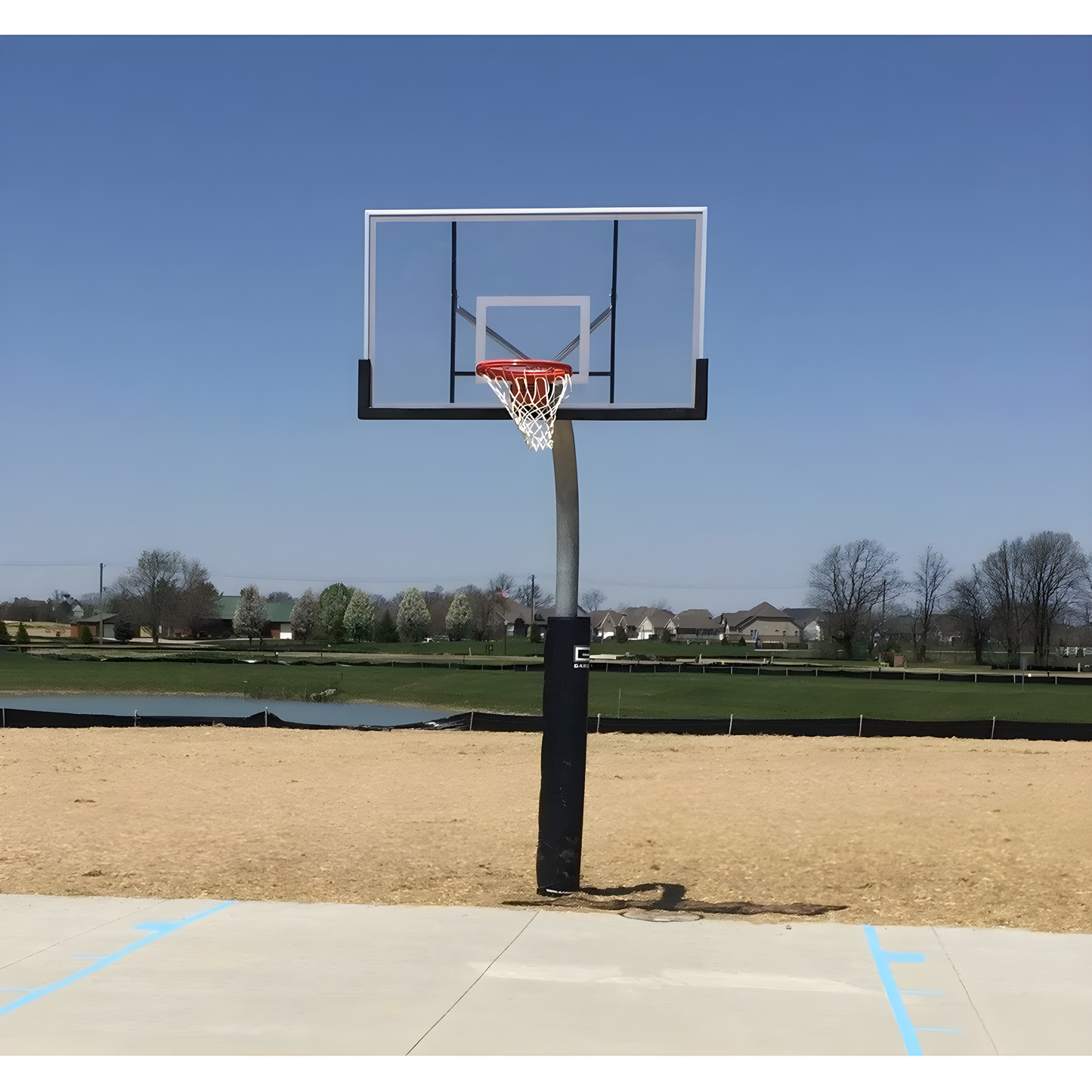 Gared outdoor basketball hoop with clear backboard and red rim on concrete court near open field