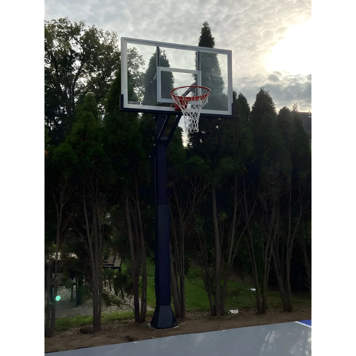 Ironclad In Ground Basketball Hoop with clear backboard and red rim installed outdoors near trees