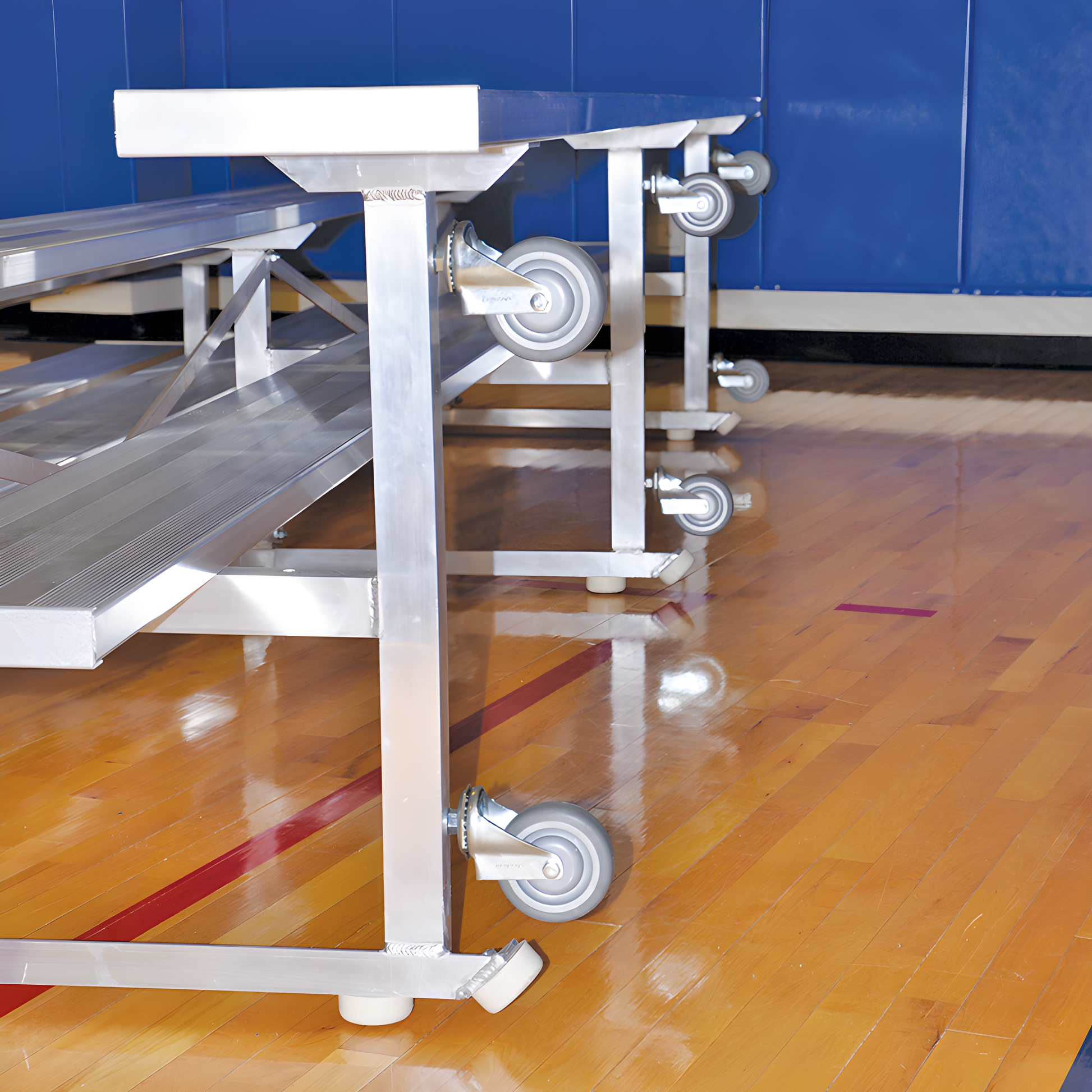 Aluminum gym bleachers with wheels on polished wooden sports floor.
