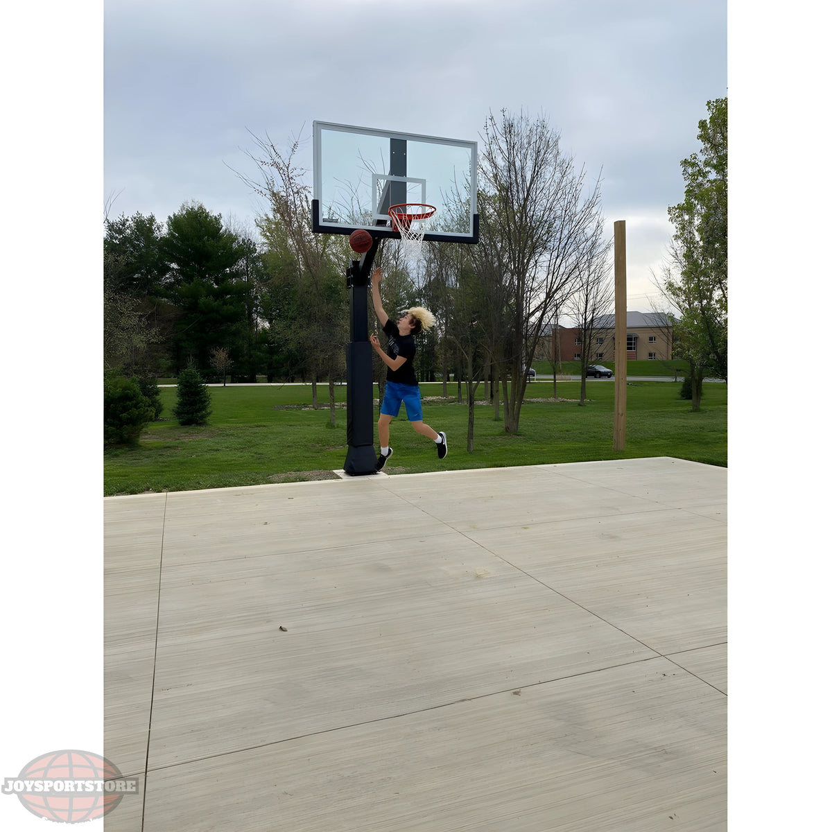 Ironclad Basketball Hoop with a player jumping to make a dunk outdoors in a park-like setting