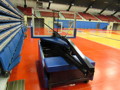 FIRST TEAM portable basketball hoop folded and stored beside seating in an indoor basketball court